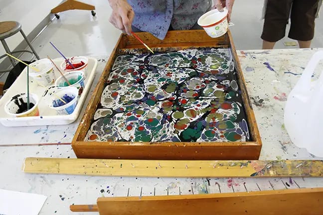 marbler spraying paint over paper marbling tray